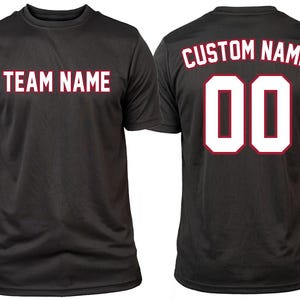 May include: Black athletic t-shirt with the text "TEAM NAME" across the front in white letters with a red outline. The back of the shirt displays "CUSTOM NAME" above the number "00" in white with a red outline. The shirt has short sleeves.