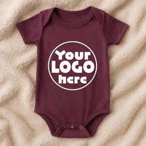 Może przedstawiać: Bordowe body dla niemowląt z kr&oacute;tkimi rękawami i okrągłym dekoltem. Body posiada napis "Your LOGO here" w białym okrągłym wzorze z przodu. Body ma trzy zatrzaski na dole.