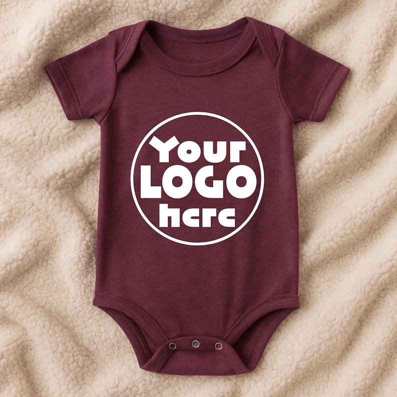Może przedstawiać: Bordowe body dla niemowląt z kr&oacute;tkimi rękawami i okrągłym dekoltem. Body posiada napis "Your LOGO here" w białym okrągłym wzorze z przodu. Body ma trzy zatrzaski na dole.