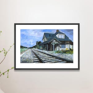 Può includere: Dipinto incorniciato di una stazione ferroviaria con tetto blu e rivestimento bianco. L'opera raffigura un binario che conduce all'edificio sotto un cielo blu nuvoloso. Il dipinto è in una cornice nera.