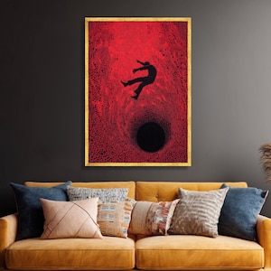 May include: A framed art print shows a silhouetted figure falling into a black hole against a textured red background. The artwork is encased in a gold-coloured frame, creating a striking contrast. The overall theme is abstract and thought-provoking.