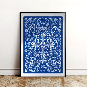 May include: A framed art print featuring a detailed, symmetrical design in white against a vibrant blue background. The artwork showcases an ornate pattern of swirling vines, leaves, and floral elements, creating a classic, elegant aesthetic.