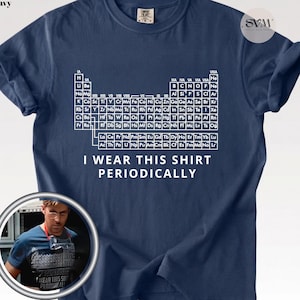 May include: A true navy blue short-sleeve t-shirt featuring a white graphic of the periodic table of elements printed on the chest. Below the table, the text reads I WEAR THIS SHIRT PERIODICALLY in white capital letters. The shirt has a crew neckline.