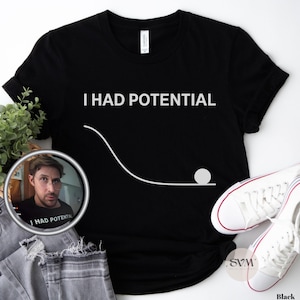 May include: A black short-sleeved t-shirt featuring the white text I HAD POTENTIAL above a white graphic of a downward curve with a circle at the bottom. The shirt is displayed alongside a pair of white canvas sneakers and grey denim jeans.