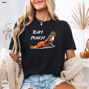 May include: Black t-shirt with the text "TEAM PUNCH" in white. The graphic depicts two monkeys, one punching the other. The shirt is made of a soft material.