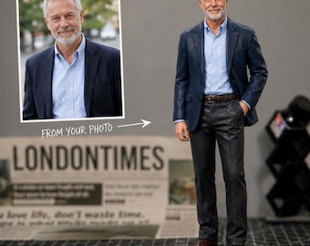 May include: A 3D-printed figurine of a man in a navy blue blazer, light blue shirt, and grey trousers. The figurine is standing next to a framed photo of the same man. The text "FROM YOUR PHOTO" and "LONDONTIMES" are visible.