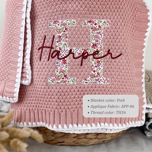 May include: A pink knitted blanket featuring a large letter H applique in a floral pattern with the name Harper embroidered in dark red script across the center. The blanket has a white crocheted border and a label listing Blanket color: Pink, Applique Fabric: APP-06, and Thread color: TH36.