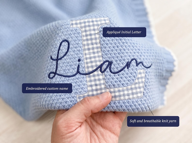 May include: A light blue knit blanket featuring a large white and blue gingham appliqu&eacute;d initial letter L with the name Liam embroidered in dark blue cursive script. The blanket is made of a textured knit yarn and includes labels pointing to the Appliqu&eacute; Initial Letter, Embroidered custom name, and Soft and breathable knit yarn.