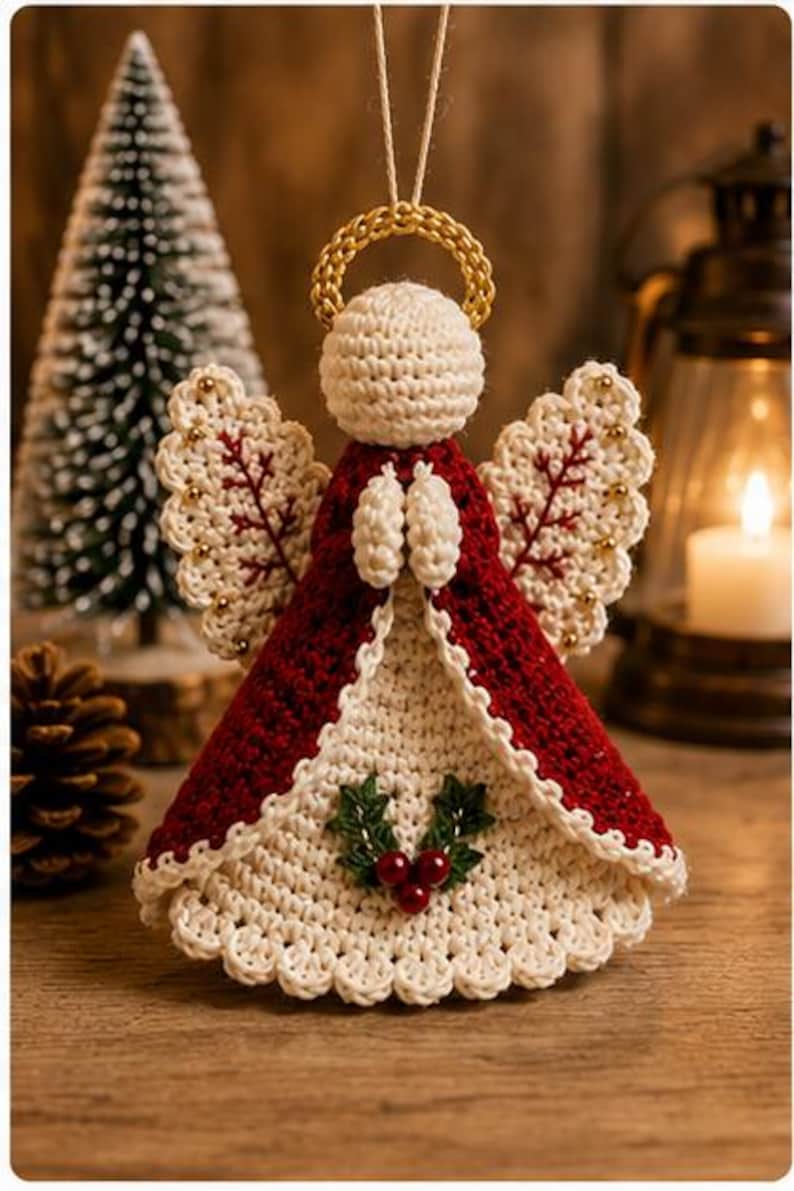 May include: A crocheted angel ornament featuring a cream-colored head and base, a deep red cloak, and a gold halo. The wings are cream with red stitching and small gold beads. A holly sprig with three red berries is centered on the front.