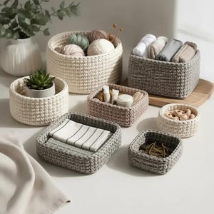 Puede incluir: Una colección de cestas de almacenamiento tejidas a ganchillo en formas redondas y cuadradas, con tonos neutros de crema, beige y gris. Las cestas contienen artículos como ovillos de lana, textiles doblados, una pequeña suculenta y cuentas de madera.