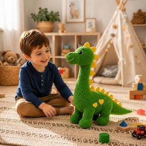 May include: A green crocheted dinosaur plush toy with a long neck, yellow spikes along its back, and two yellow heart-shaped patches on its side. The dinosaur has a stitched smile and black eyes, standing upright on a textured rug in a room.