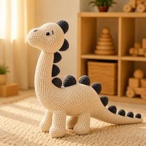May include: A crochet dinosaur toy made with cream-colored yarn for the body and dark gray yarn for the spikes along its back and head. The dinosaur has a long neck, a rounded snout, and two black plastic eyes, standing on four sturdy legs.