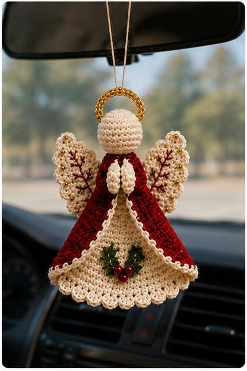 May include: A crocheted angel ornament hanging from a string, featuring a cream-colored head and halo, a deep red dress with cream trim, and wings with red stitching. The front of the dress is decorated with a small green holly and red berry motif.