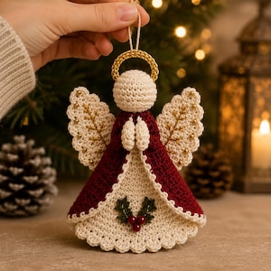 May include: A crocheted angel ornament featuring a cream-colored head with a gold halo, a deep red outer robe, and a cream-colored inner dress. The wings are cream with gold embroidery and beads, and the front displays a holly leaf and berry motif.