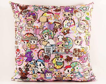May include: A square throw pillow featuring a light pink background covered in a colorful pattern of cartoon characters, donuts, cupcakes, popcorn, and stars. The design includes various small figures with large eyes and diverse food-themed accessories.