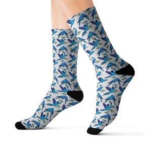 Op de afbeelding: Crew sokken met een herhalend patroon van blauwe vogels en groene bladeren op een witte achtergrond. De sokken hebben zwarte hielen en tenen. De sokken zijn gemaakt van een zacht, comfortabel materiaal.
