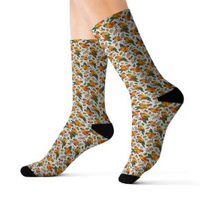 May include: A pair of socks with a repeating pattern of orange, yellow, and green birds and foliage on a white background. The socks have black heels and toes. The socks are knee-high.