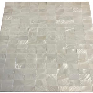 Puede incluir: Superficie cuadrada compuesta por numerosos azulejos rectangulares blancos iridiscentes, dispuestos en un patrón de mosaico. Los azulejos crean una superficie texturizada y reflectante. El efecto general es un aspecto brillante y nacarado.