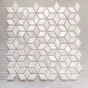 May include: White mother-of-pearl mosaic tile sheet with a geometric 3D cube design. The tiles are arranged in a honeycomb pattern, creating a textured surface. The mosaic is suitable for various interior design applications.