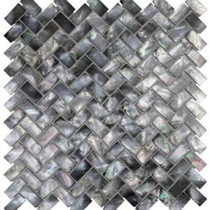 Może przedstawiać: Mozaika w jodełkę w odcieniach szarości, czerni i opalizującej perły. Prostokątne płytki ułożone są w zygzakowaty wzór, tworząc teksturowaną powierzchnię. Płytki mają błyszczące wykończenie, odbijające światło i dodające głębi wzornictwu.