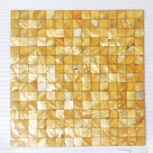 May include: Square mosaic tile with a shimmering, golden-yellow mother-of-pearl finish. The tile is composed of numerous small, square pieces, creating a textured surface. The overall effect is a luxurious and elegant design.