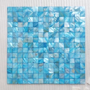 May include: Square mosaic tile sheet composed of small, iridescent blue and white tiles. The tiles are arranged in a grid pattern, creating a shimmering, textured surface. The overall effect is a cool, aquatic aesthetic, suitable for various decorative applications.