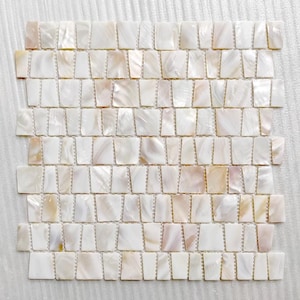 Könnte beinhalten: Eine Mosaikfliesenplatte mit vielen kleinen, rechteckigen Fliesen. Die Fliesen haben eine perlmuttartige, cremeweiße Farbe mit subtilen Variationen von Rosa und Beige. Die Fliesen sind in einem Raster angeordnet, geeignet für Inneneinrichtung.