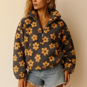 May include: A gray fleece pullover with a yellow floral pattern. The pullover has a high collar, a quarter-zip closure, and a front pocket. The model is wearing denim shorts.