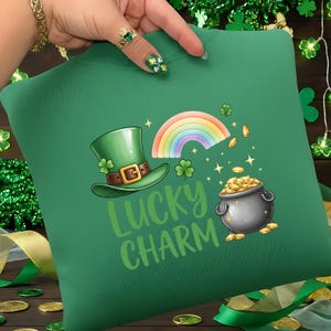 Puede incluir: Sudadera verde con un diseño del Día de San Patricio. El gráfico incluye un sombrero verde de duende, un arcoíris, una olla de oro y las palabras "Lucky Charm". El diseño también presenta tréboles y monedas de oro.