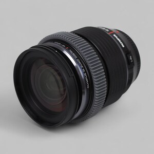 以下が含まれることがあります： 黒いオリンパスM.Zuiko Digital 12-40mm f/2.8 PROレンズ。レンズには「OLYMPUS M. ZUIKO DIGITAL 12-40mm」の文字が入ったシルバーリングと、グレーのテクスチャードグリップが付いています。プロの写真撮影用に設計されています。