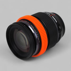 以下が含まれることがあります： オレンジ色のリブ付きフォーカスリングが付いた、黒色のオリンパスM.Zuiko Digital 12-40mmレンズ。レンズには「OLYMPUS M. ZUIKO DIGITAL 12-40mm」の文字がプリントされたシルバーリングが付いています。写真撮影用に設計されています。