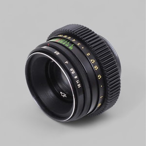 Peut inclure: Un objectif d'appareil photo noir avec une bague de mise au point striée et des marquages d'ouverture en jaune et blanc. L'objectif a un anneau argenté autour de l'élément avant et diverses marques numériques.