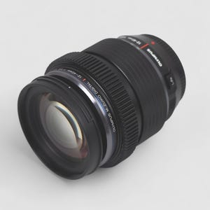 以下が含まれることがあります： 黒色のオリンパスM.Zuiko Digital 12-40mm f/2.8 PROレンズ。レンズには「Olympus M.Zuiko Digital 12-40mm」の文字が入ったシルバーリングと黒いレンズフードが付いています。レンズはわずかに左に傾いています。