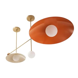 May include: Contemporary ceiling light fitting featuring an orange oval shade with a white globe. The fixture has a brass finish with two additional lights, one with a round shade and the other a white globe.