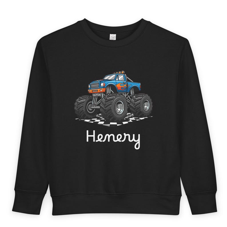 May include: Black sweatshirt featuring a blue monster truck graphic with orange flames and large black tires. The name "Henery" is written in white script below the truck. The truck is on a checkered pattern.