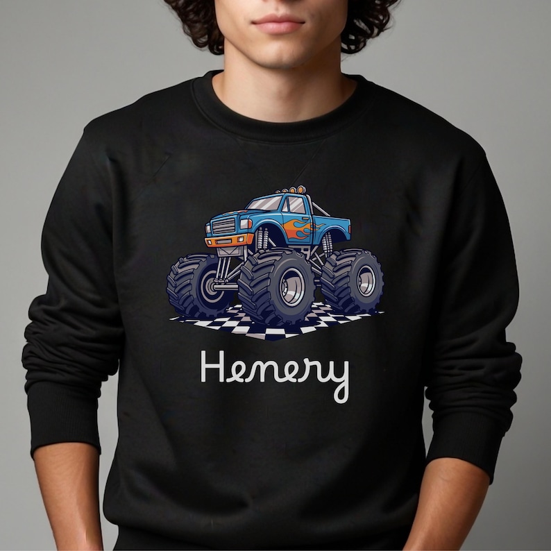 May include: Black sweatshirt featuring a blue monster truck graphic with orange flames and large tires. The name "Henery" is written in white script below the truck. The truck is on a checkered pattern.