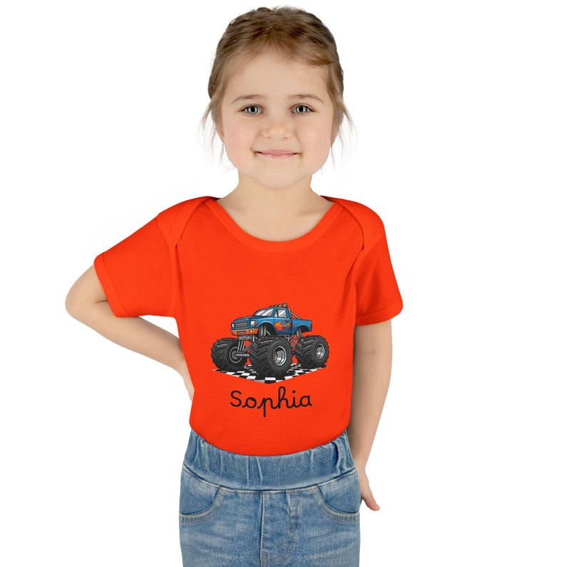 May include: An orange baby bodysuit featuring a blue monster truck graphic with flames and large tires. The name "Sophia" is written in cursive below the truck. The bodysuit is short-sleeved and made of a soft material.