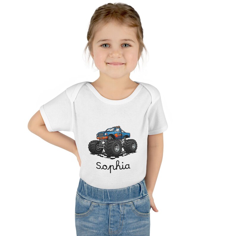 May include: White baby bodysuit featuring a blue monster truck graphic with large black tires. The name "Sophia" is written in cursive below the truck. The bodysuit is worn by a young child.