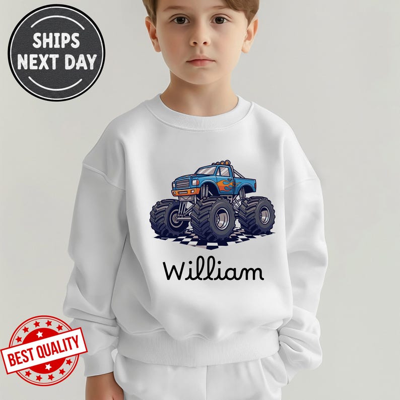 May include: White sweatshirt featuring a blue monster truck graphic with orange flames and the name "William" in black script. The truck is on a checkered pattern. The sweatshirt has a crew neck.