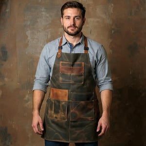 Könnte beinhalten: Eine dunkelgrüne Schürze mit braunen Ledertaschen und -riemen. Die Schürze hat mehrere Taschen und ein robustes, abgenutztes Aussehen. Die Lederriemen sind mit Metallnieten befestigt. Die Schürze ist für Arbeits- oder Bastelaktivitäten geeignet.