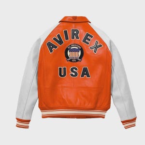 Puede incluir: Chaqueta de cuero naranja y blanca con el texto "AVIREX" y "USA" en la espalda. La chaqueta tiene mangas blancas y un dobladillo a rayas. También es visible un parche con las palabras "ALL AMERICANS" y "ESTABLISHED 1975".