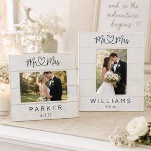 May include: Two white wooden picture frames with a horizontal plank design. Each frame features the text Mr & Mrs, a heart icon, a surname, and a date. The left frame displays the name PARKER and 5.18.26, while the right frame displays WILLIAMS and 9.21.26.