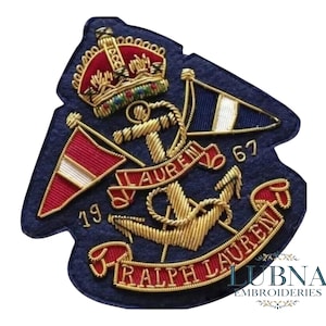 Könnte beinhalten: Marineblau gestickter Aufnäher mit goldener Anker, Krone und Flaggen. Der Aufnäher enthält den Text "RALPH LAUREN" und die Zahlen "19" und "67". Das Design ist mit roten, weißen und goldenen Akzenten versehen.
