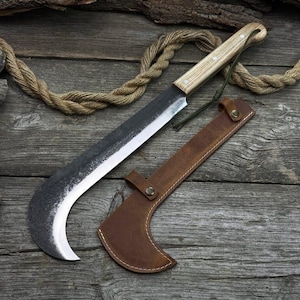 Könnte beinhalten: Ein großes Messer mit gebogener Klinge, hellem Holzgriff und brauner Lederscheide. Die Klinge hat eine dunkle, strukturierte Oberfläche mit einer scharfen, silbernen Schneide. Eine grüne Schnur ist am Griff befestigt. Messer und Scheide liegen auf einer Holzoberfläche.