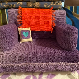 May include: A purple crocheted armchair with a crocheted orange throw pillow and a white pillow with a blue heart on it.