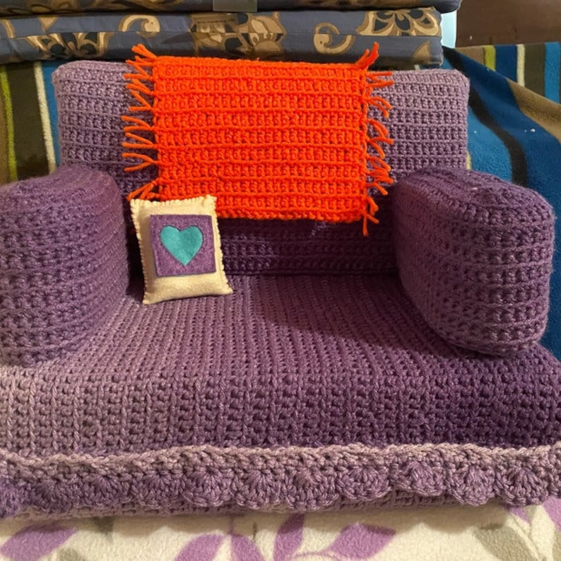 May include: A purple crocheted armchair with a crocheted orange throw pillow and a white pillow with a blue heart on it.