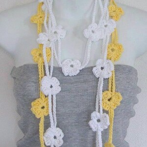May include: A white and yellow crocheted flower necklace. The necklace is made of multiple strands of crocheted flowers, with some flowers being white and others being yellow.