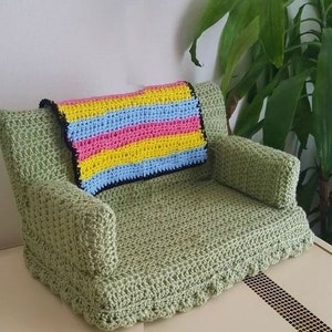 May include: A green crocheted couch with a multi-colored striped throw pillow. The couch has a crocheted fringe around the bottom.
