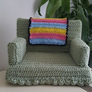 May include: A green crocheted armchair with a striped crocheted cushion in pink, yellow, and blue.