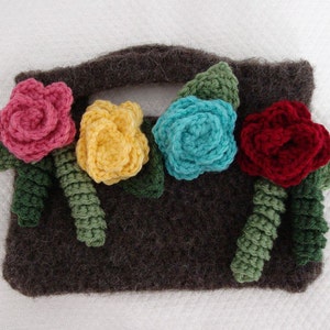 May include: A brown crocheted bag with a handle and four crocheted flowers in pink, yellow, blue, and red.
